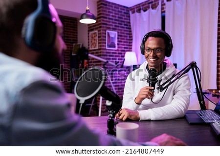 Multiethnic team of people meeting to record podcast episode together, creating online content with live broadcast discussion. Male vlogger talking to adult, livestream production. Royalty-Free Stock Photo #2164807449