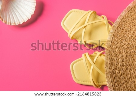Pair of women's yellow strappy sandals with straw hat and sea shell isolated on a pink background. Beach accessories. Summer vacation concept.