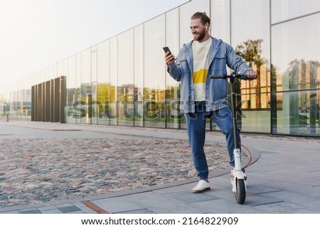 Young cheerful man with e-scooter using scooter-sharing system application on his smartphone Royalty-Free Stock Photo #2164822909
