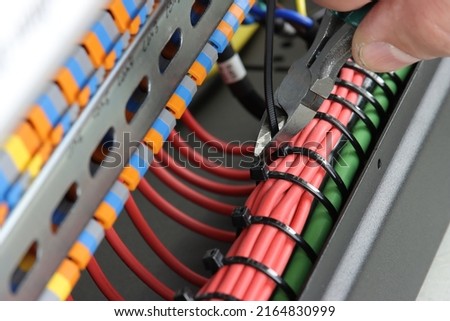 Cutting plastic cable ties on insulated wire with wire cutters. Close-up. Royalty-Free Stock Photo #2164830999