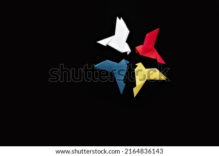 four paper origami pigeons white, red, blue and yellow on black background