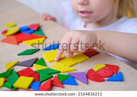 Litle cute child, girl plays with colored wooden geometric figures, cubes, builds houses and animals, counts details, concept of development of creativity, fine motor skills, patience perseverance Royalty-Free Stock Photo #2164836211