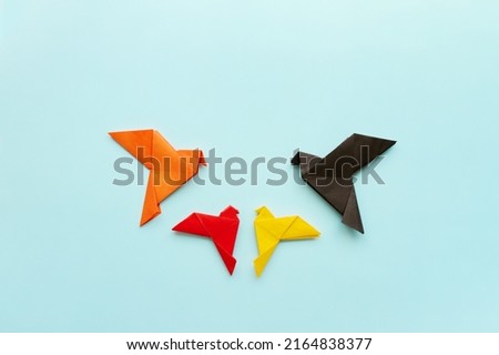 four paper origami pigeons black, orange, red and yellow on light blue background