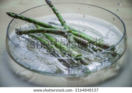 Water washing of levitating vegetable fresh asparagus. Asparagus in a bowl of splashing water. Greenery bought at farmer's market. Food high on vitamins.