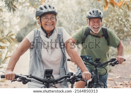 Two happy old mature people enjoying and riding bikes together to be fit and healthy outdoors. Active seniors having fun training in nature. Royalty-Free Stock Photo #2164850313
