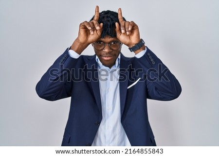 Young african man with dreadlocks wearing business jacket over white background doing funny gesture with finger over head as bull horns 