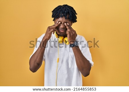 Young african man with dreadlocks standing over yellow background rubbing eyes for fatigue and headache, sleepy and tired expression. vision problem 