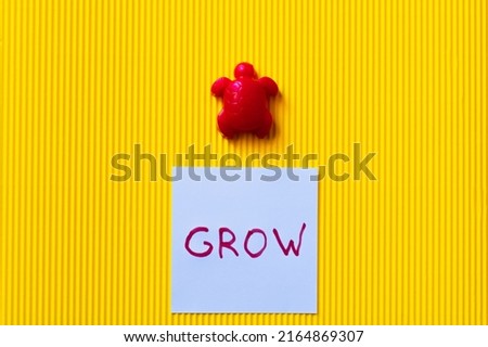 top view of blue card with grow lettering near red toy turtle on yellow background