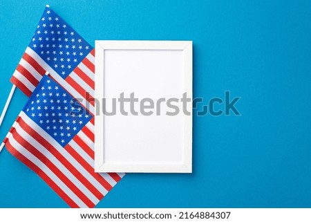 USA Independence Day concept. Top view photo of white photo frame and national flags on isolated blue background with copyspace