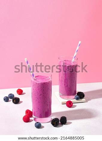 Two glasses of purple wild berry smoothie or milkshake on pink pastel background, copy space for text. Healthy breakfast drink Royalty-Free Stock Photo #2164885005