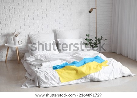 Interior of light bedroom with flag of Ukraine and comfortable bed