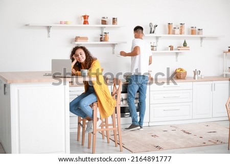 Young African-American woman using laptop at table in kitchen