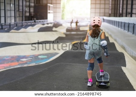 back asian child or kid girl playing surf skate or skateboard and start on indoor pump track in skatepark by extreme sports to wearing helmet elbow pads wrist and knee support for body safety protect Royalty-Free Stock Photo #2164898745