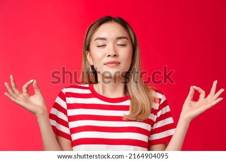 Girl feeling zen. Cute asian girl meditating unite with nature, close eyes breathing deep hold hands raised lotus nirvana pose, practice yoga, inhale air, release stress, calm-down red background Royalty-Free Stock Photo #2164904095