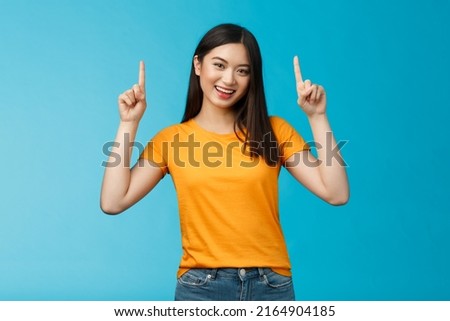 Lively asian girl dark short haircut, tilt head cute smile camera, raise hands and pointing index fingers up, introduce top promo, grinning, bragging new cool purchase, stand blue background Royalty-Free Stock Photo #2164904185