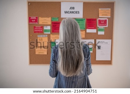 Job center employee standing in front of employment noticeboard. Rear view. Royalty-Free Stock Photo #2164904751