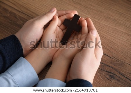 Boy and his godparent holding cross at wooden table, closeup