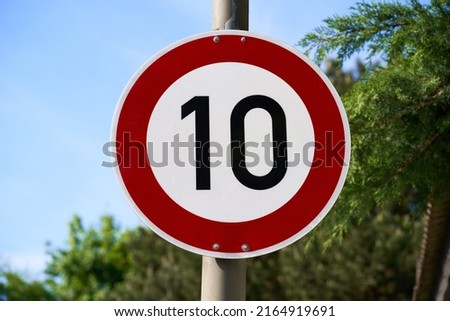 A traffic sign indicating that the speed limit is 10 kmh or 10 mph. Blue sky and trees out of focus in the background.                             