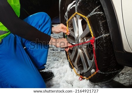 Close-up of man's hands putting on chains on the car wheel on the icy road at winter mountains Royalty-Free Stock Photo #2164921727