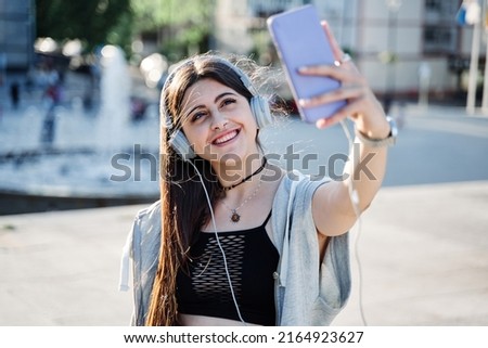 young teenager taking a selfie with a mobile phone. woman with headphones making a video call in the city.