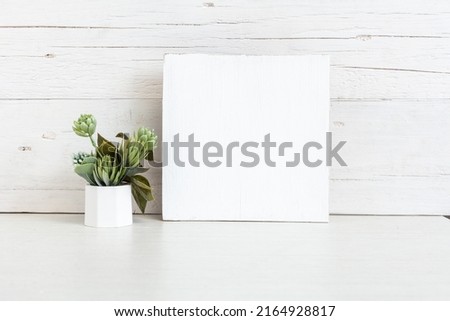 Mockup of a white wooden sign. White square sign on the table with a flower.