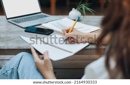 Young asian woman in casual clothing working at outdoor cafe, using laptop computer working or study with paperwork on wooden table