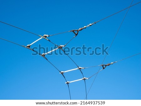 Overhead catenary and contact wires for an electric trolley bus system on a bend with a plain blue sky background.