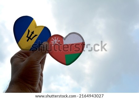 Hand holds a heart Shape Barbados and Oman flag, love between two countries