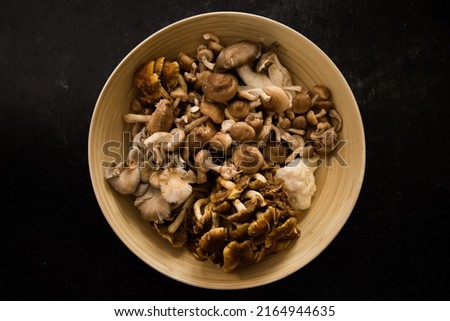 Mixture of wild lion's mane, oyster, cinnamon cap and shiitake mushrooms in bamboo bowl on dark black background. Royalty-Free Stock Photo #2164944635