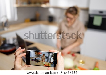 Daughter with smartphone filming her mother while cooking in the kitchen