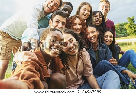 Cheerful international happy friends having fun taking selfies at picnic in the countryside - Large group of multiethnic young people smiling looking at the camera - focus on the black woman face