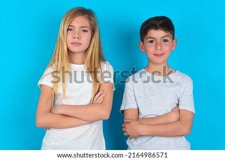 two kids boy and girl standing over blue background frowning his face in displeasure, keeping arms folded, waiting for an explanation.