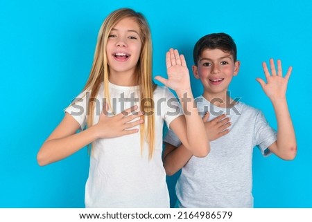I swear, promise you not regret. Portrait of sincere two kids boy and girl standing over blue background raising one arm and hold hand on heart as give oath, telling truth, want you to believe. Royalty-Free Stock Photo #2164986579
