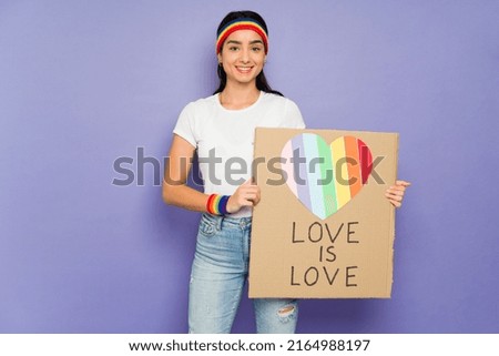 Portrait of a happy gay woman smiling while showing a Love is Love banner and supporting LGBT+ rights 