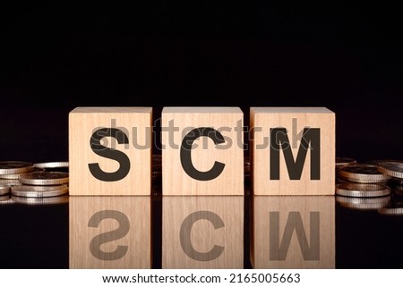 scm - text on wood blocks on black background with coins. front view. business concept