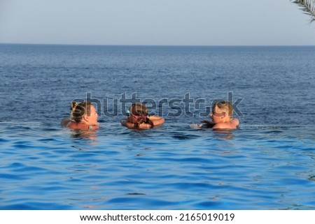 woman, a girl and a boy swim in the pool against the background of the sea.