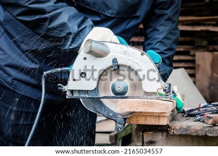 a carpenter is engaged in sawing boards with a circular saw at their summer cottage Royalty-Free Stock Photo #2165034557