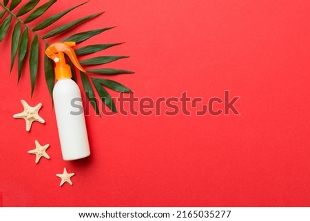 Sunscreen spray bottle. Bottle with sun protection cream and sea shells with tropical green leaf on color background, top view.