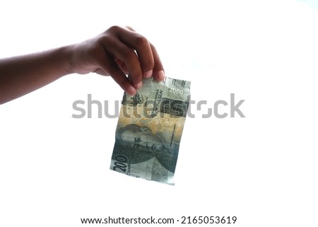 a hand holding two thousand rupiah worth of Indonesian currency on a white background