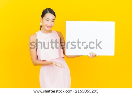 Portrait beautiful young asian woman with empty white billboard on yellow color background