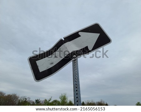 An arrow street sign that is now bend and crooked from wear. The damaged metal sign is now pointing to the sky.