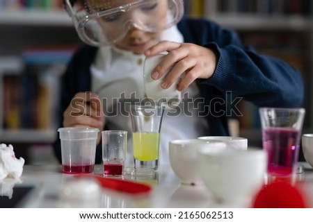 Close up on hand of One small caucasian boy scientist five years old sitting at the table playing with chemistry equipment toy preforming experiment learning and education concept front view