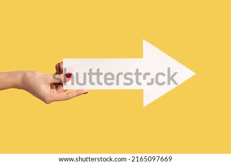 Closeup profile side view of woman hand showing white arrow in hands indicating aside, showing right direction. Indoor studio shot isolated on yellow background.