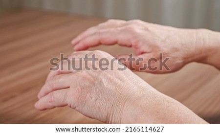 Old woman trembling hands due to Parkinson disease. Lady with shakiness holds wrinkled hands over table. Elderly female hands tremor closeup Royalty-Free Stock Photo #2165114627