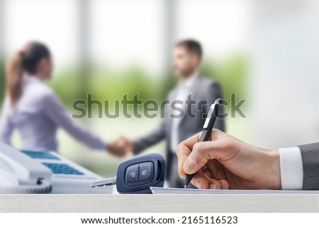Customer and car salesman shaking hands at the car dealership, businessman signing a contract in the foreground Royalty-Free Stock Photo #2165116523