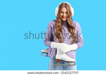 Beautiful young woman with ice skates on blue background