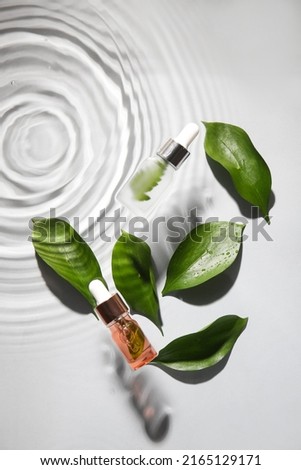 Bottles of natural serum and plant leaves in water on white background