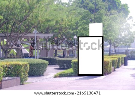 Vertical blank advertising poster billboard banner mockup; lush plants and tress in background; digital light box display screen for OOH out of home media