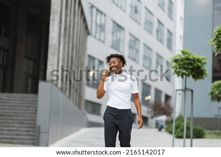 Photo of amazing pretty african american lady, spending time walking on city street after university lectures, holding telephone while speaking with best friend.