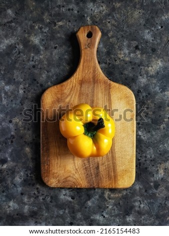 Yellow sweet bell pepper on wooden cutting board on black concrete background with copy space. Rustic flatlay with summer vegetable.